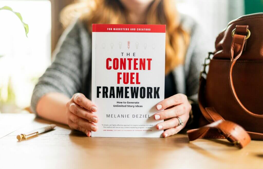woman holding a book titled "The Content Fuel Framework: How to Generate Unlimited Story Ideas"
