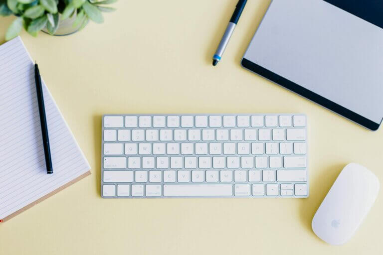 Yellow Desk with plant, pad and pen, keyboard, mouse, laptop all ready to research website design services and find the website design agency for their next project